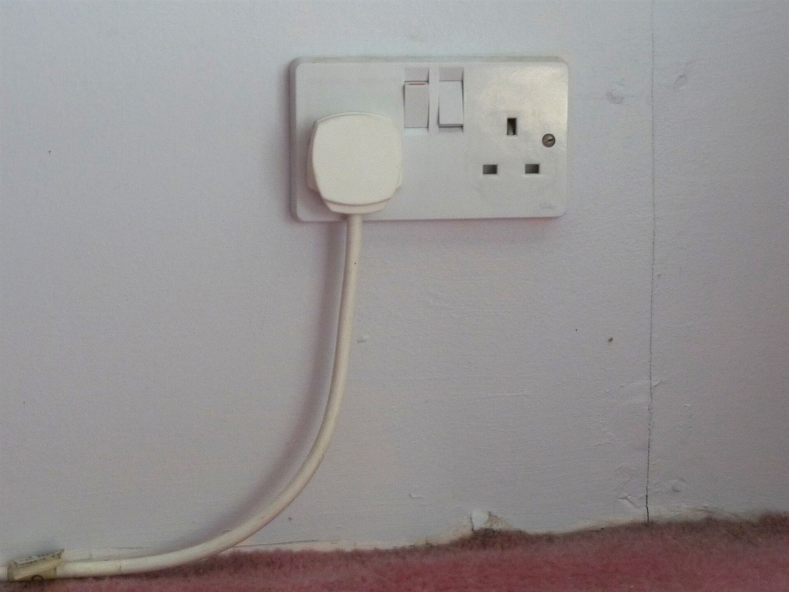 A UK double wall socket with a plug in use