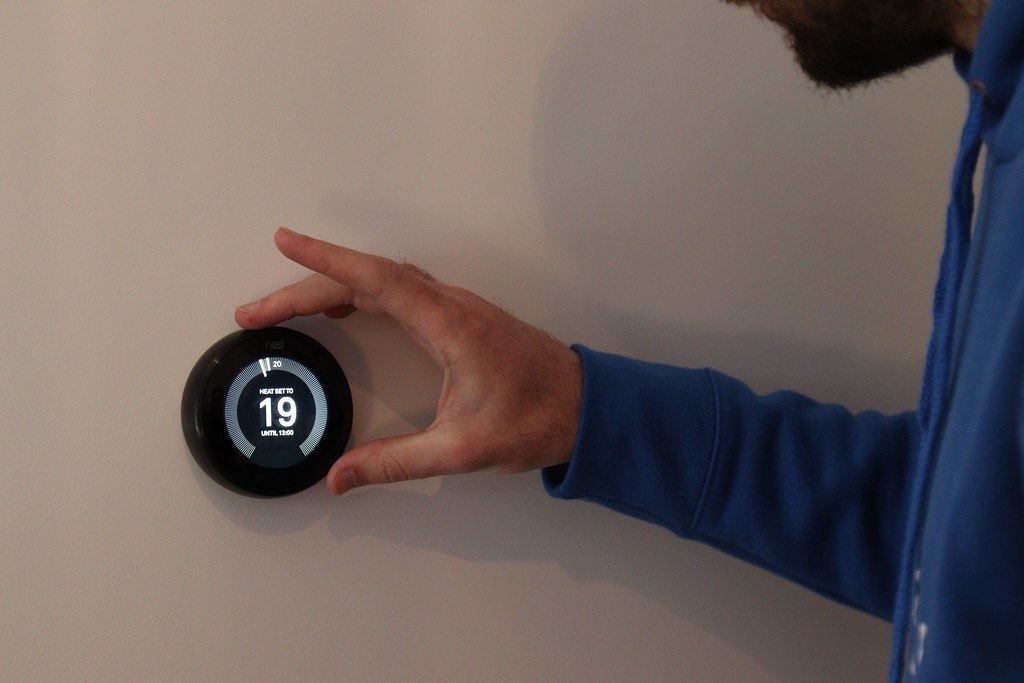 A hand turning a smart thermostat on a living room wall